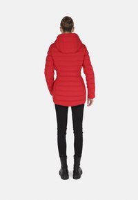 Chaqueta acolchada roja con cintura entallada y capucha, con una textura acolchada. Combinada con pantalones negros ajustados y botas negras gruesas.