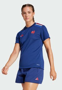 Navy athletic shirt with red rooster logo, white and red striped accents on shoulders, paired with navy shorts featuring red Adidas logo.