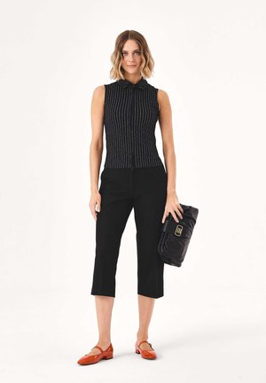 Sleeveless black top with vertical white stripes, paired with black cropped pants. Model holds a shiny black clutch and wears orange flats.