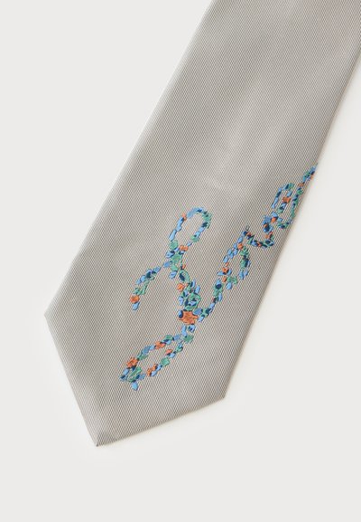 Cravate rayée gris clair avec un mot brodé floral en fils bleu, vert et orange près de l'extrémité pointue.