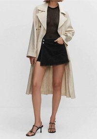 Abrigo largo beige, top negro de canalé, falda de mezclilla negra con botones y sandalias de tacón alto negras con tiras. Diseño minimalista.
