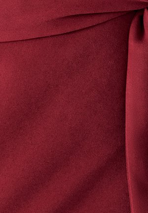 Bordeaux stof med en glat tekstur og let glans, der har bløde folder og draperinger, som skaber subtil visuel interesse.