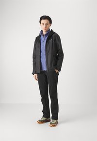 Black waterproof jacket, purple zip-up fleece underneath, black pants, and olive green sneakers with orange accents. Simple, functional design.