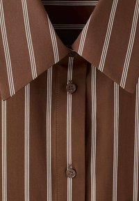 Brauner Hemdkragen mit vertikalen weißen Streifen und zwei braunen Knöpfen entlang der Knopfleiste, zeigt Stoffstruktur und Nähdetails.