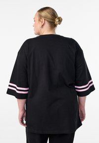 Black oversized t-shirt with short sleeves, featuring pink stripes on the cuffs. Fabric is smooth cotton with a relaxed fit and longer back.
