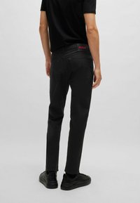 Sorte denimbukser med slim fit, prydet med et karakteristisk rødt logo på linningen og enkle baglommer. Glat tekstur og subtil syning.