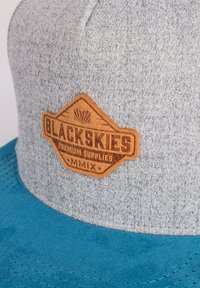 Hallhalli hallitav suvine kihara, millel on sinine nahkbrim, sisseprinditud nahast logo silt "BLACKSKIES PREMIUM SUPPLIES MMIX" detailidega.