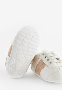 Zapatos de bebé blancos con rayas de ante marrón claro, punteras redondas, suelas de goma texturizadas y cordones. Acabado de piel suave con acentos en forma de onda.