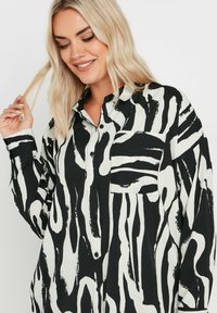 Black and white button-up shirt with an abstract wave pattern, featuring a breast pocket and long sleeves. Smooth fabric with a relaxed fit.