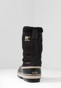 Botas negras impermeables con un upper de tela texturizada, cuello forrado de piel y suela de goma. Presenta la marca Sorel y una cinta de agarre.