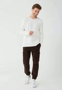 White long-sleeve t-shirt paired with dark brown cargo pants and white sneakers. Soft fabric with a relaxed fit; pants have side pockets.