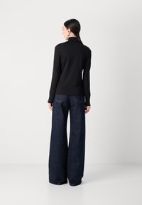 Zwarte lange mouwen top met hoge hals, gecombineerd met donkere wijd-uitlopende jeans met een klassiek achterzakdesign en zichtbare naden.