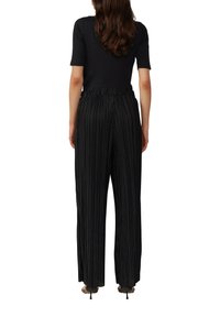 Pantalon noir plissé avec une taille élastique, jambes larges et finition texturée. Associé à un haut noir ajusté et des chaussures à talons.