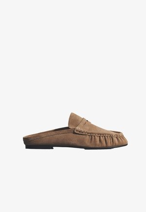 Hnedý semišový mokasín typu slip-on s plochou čiernou podrážkou a šitím v štýle mokasínu okolo oblasti špičky.