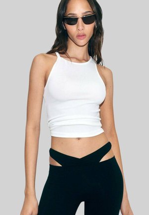 White ribbed tank top paired with black high-waisted leggings featuring cut-out accents. Model wears narrow black sunglasses.