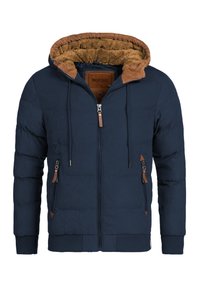 Veste matelassée bleu marine avec une capuche doublée en polaire marron, fermeture éclair frontale double et deux poches latérales avec zip. Des poignets et un ourlet élastiques complètent le design.
