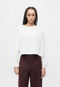 Biała, długorękawowa, krótka bluza z okrągłym dekoltem, luźnym krojem i ściągaczami przy mankietach, zestawiona z wysokim stanem bordowych spodni.