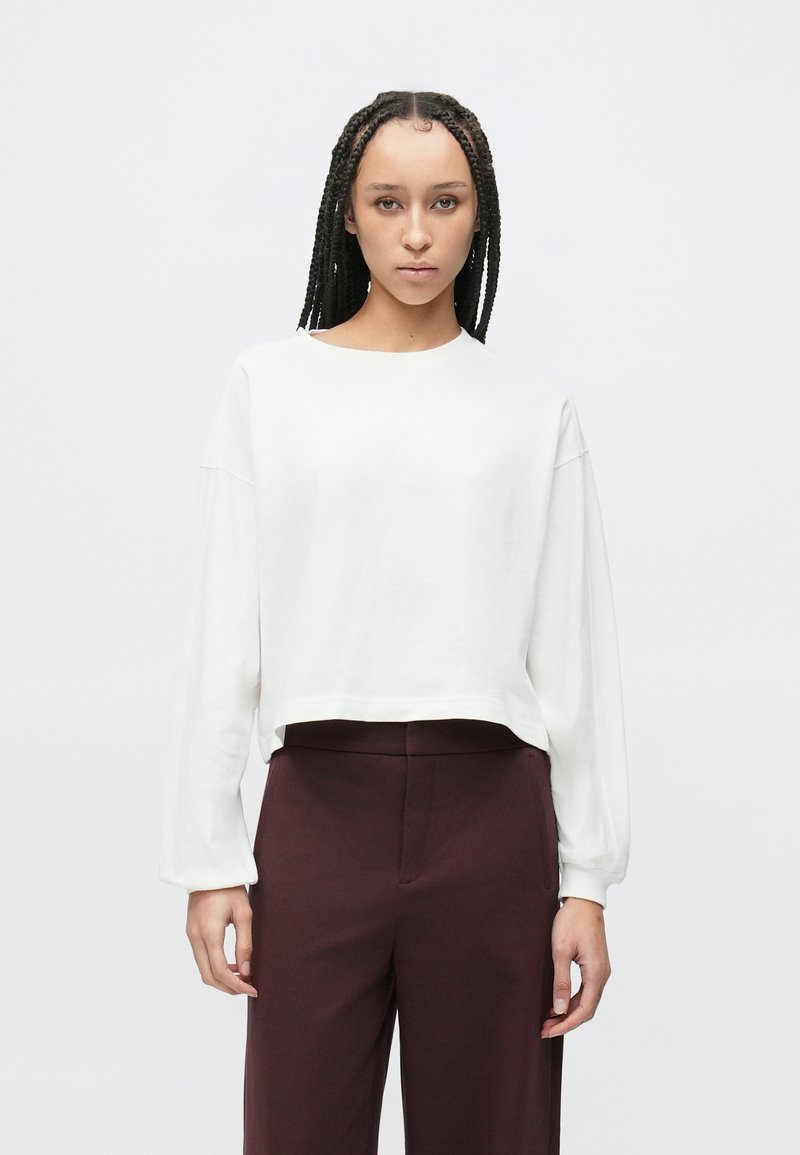 Biała, długorękawowa, krótka bluza z okrągłym dekoltem, luźnym krojem i ściągaczami przy mankietach, zestawiona z wysokim stanem bordowych spodni.