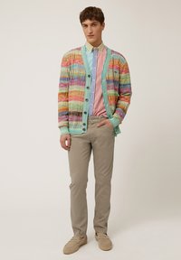 Cárdigan de punto multicolor con rayas verticales, grandes botones, usado sobre una camiseta a rayas, combinado con pantalones beige y zapatos claros.