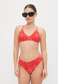 Röd bikini-set med triangulärt topp och hög midje-bakdel, prydd med vita blommönster, tillverkad av mjukt tyg. Svarta solglasögon ingår.