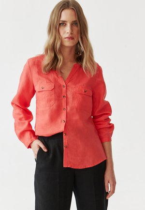 Camicia a maniche lunghe corallo con chiusura a bottoni, due tasche sul petto e scollatura a V; realizzata in tessuto leggero e dalla texture liscia.