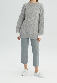 Grijze kabelgebreide trui met een ronde hals, oversized pasvorm en lange mouwen, gecombineerd met geruite cropped broek en witte sneakers.