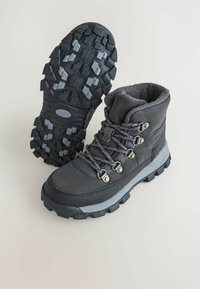 Czarne wodoodporne buty trekkingowe z teksturowanym materiałem, szarymi akcentami i wytrzymałą gumową podeszwą z głębokim bieżnikiem dla lepszej przyczepności.