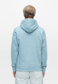 Ανοιχτό μπλε φούτερ από μαλακό ύφασμα; διαθέτει μια μεγάλη, ρυθμιζόμενη κουκούλα και ριγωτές μανσέτες. Η πλάτη έχει μια ομαλή, χωρίς ραφές σχεδίαση.