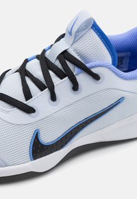 Lysblå atletisk sko med sorte snørebånd, mesh-overdel og en blå accent swoosh-logo. Har en struktureret overflade og gummisål.