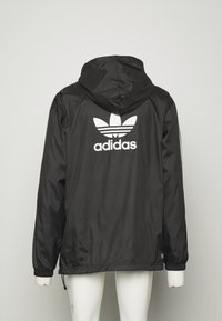 Černá voděodolná bunda s kapucí, zdobená bílým logem Adidas a třemi pruhy na rukávech. Elastické manžety a nastavitelný spodní lem.