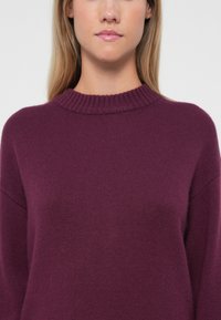Maglione viola lavorato a maglia con scollo rotondo a coste e maniche lunghe, caratterizzato da una texture morbida e una vestibilità comoda.