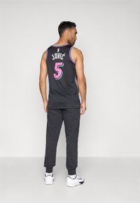 Čierna basketbalová dres s ružovými a modrými akcentmi, s menom "JOVIĆ" a číslom "5" na zadnej strane. Spárovaný s tmavými teplákmi a bielymi teniskami.