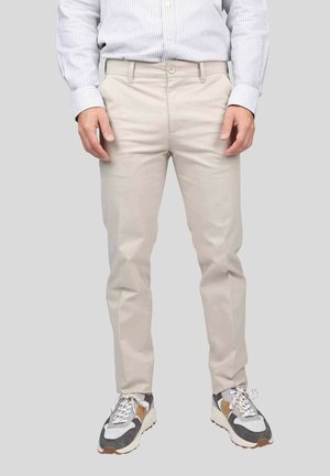 Pantalon beige clair à coupe slim, avec deux poches avant et une fermeture à bouton. Associés à des baskets multicolores avec des accents blancs, gris et marron.