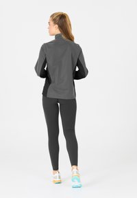 Idrottsjacka i mörkgrått med hög krage, kombinerad med åtsittande svarta leggings och vita sneakers med färgglada detaljer.