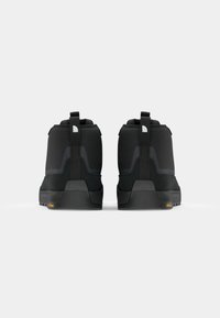 Chaussures montantes noires avec un dessus texturé, un talon renforcé et des languettes de tirage. Semelle extérieure Vibram visible en jaune contrasté.