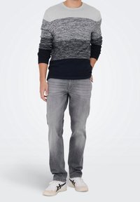 Suéter de punto con rayas horizontales en gris, azul marino y negro; jeans ajustados grises; zapatillas blancas con detalles en negro.