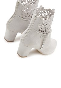 Botines de ante grises con un diseño de corte en forma de encaje en la parte superior, cremallera trasera y tacón de bloque. Presentan acentos de hardware en tono plateado.