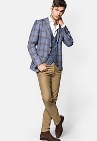Niebieska kraciasta marynarka na niebieskiej kamizelce, zestawiona z jasnobrązowymi spodniami i brązowymi zamszowymi botkami za kostkę. Marynarka posiada klapę z ząbkowanym wykończeniem i zapięcie na guziki.