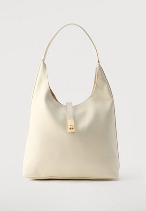 Kreminės spalvos odinė hobo rankinė su vienu peties dirželiu, lygiu paviršiumi ir priekyje auksinio tono užsegimu.