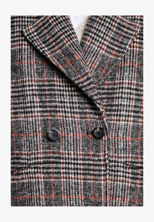 Dobbeltbrystet frakke med et sort, gråt og hvidt ternet mønster med orange accenter, lavet af struktureret stof og afsluttet med sorte knapper.
