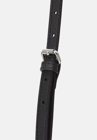 Sort læderrem med en struktureret overflade, der har en sølvmetalspænde og flere huller til justering. Simpelt og funktionelt design.