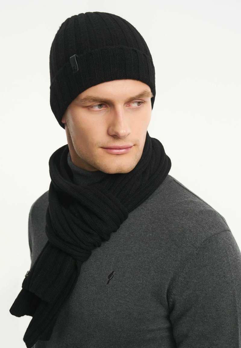 Czarna dzianinowa czapka i pasujący szalik z miękkiego materiału. Żebrowana tekstura o gładkim wykończeniu, noszone na ciemnoszarym golfie.