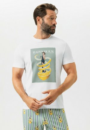 Mann trägt weißes T-Shirt mit Vintage-„Happy Hour“-Grafik einer Frau mit Getränk, Zitronenscheibe und Spiralschale, kombiniert mit gestreiften Shorts.