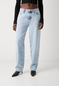 Lyseblå denim vide bukser med høy livhøyde, beltehemper og en falmet vask. Kombinert med svarte spisse hæler.