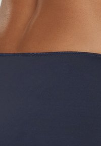 Granatowy materiał kostiumu kąpielowego o gładkiej fakturze, z bezzszywanym górnym brzegiem i minimalnym szwem, prezentujący dopasowany krój.