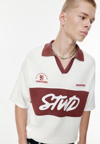 Kortærmet polo skjorte i hvid med maroon detaljer. Har V-hals, broderede logoer og en tekstureret stof. Casual design.