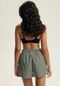 Czarno-białe szorty w kratę gingham z elastycznym paskiem w talii, o swobodnym kroju i długości do kolan. Widok z tyłu.