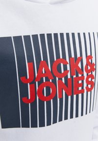 Felpa bianca con un motivo audace caratterizzato da strisce nere e il testo "JACK & JONES" in font rosso al centro.