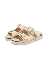 Sandalias beige con dos hebillas ajustables, una suela plana y una plantilla texturizada. Cuenta con un pequeño acento de logo rosa en el lateral.