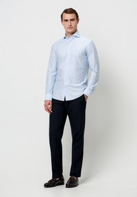 Lichtblauw gestreept overhemd met lange mouwen, getailleerd ontwerp en knoopsluiting. Gecombineerd met donkere broek en zwarte schoenen, voorkant gezien.